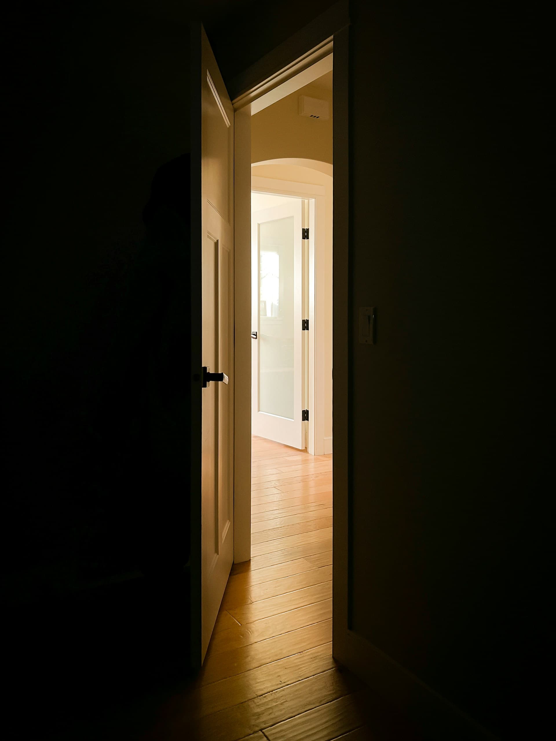 A wooden door slightly ajar with warm morning light spilling through into a quiet hallway