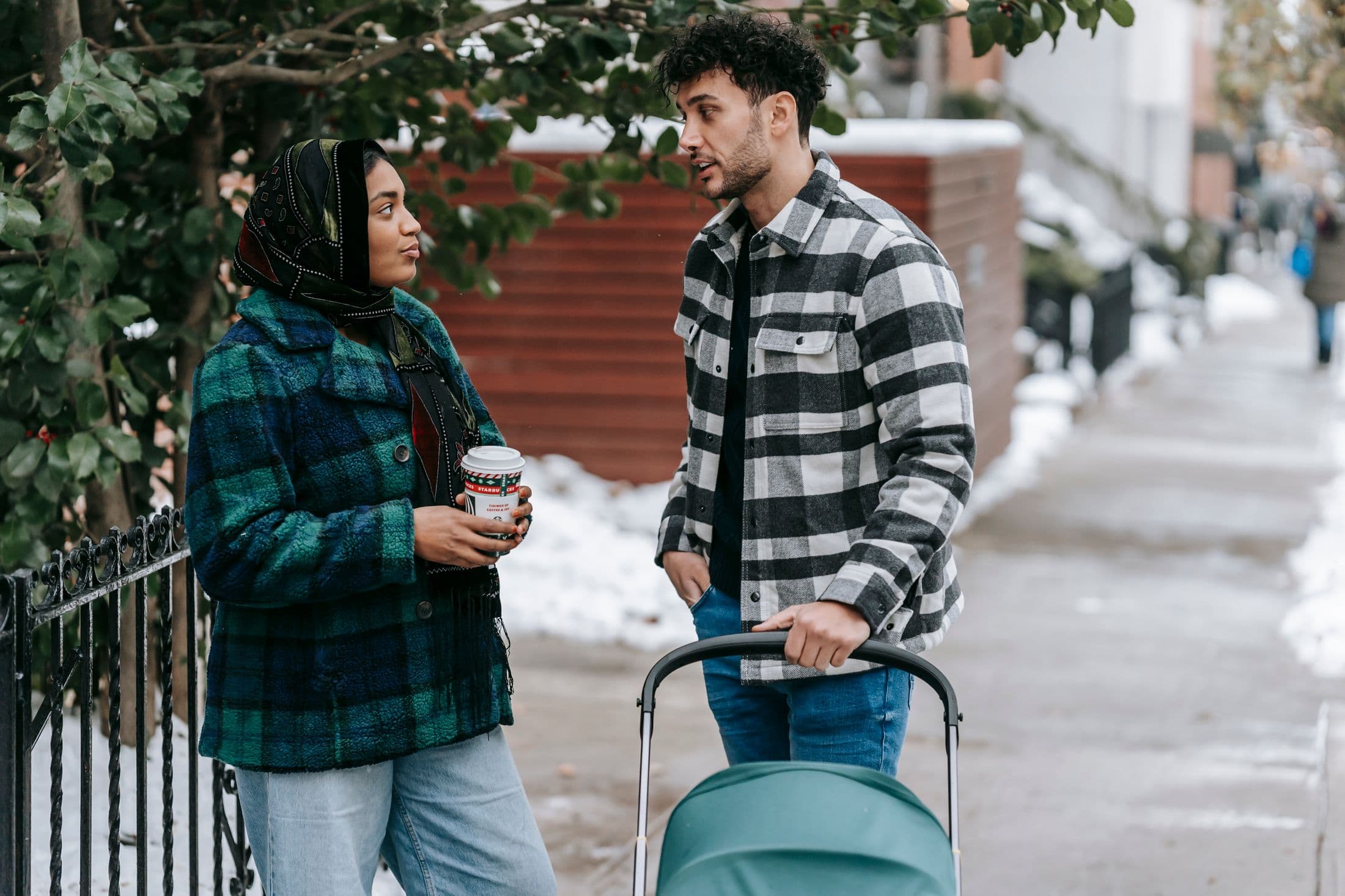 Two parents talking on a snowy sidewalk with a stroller
