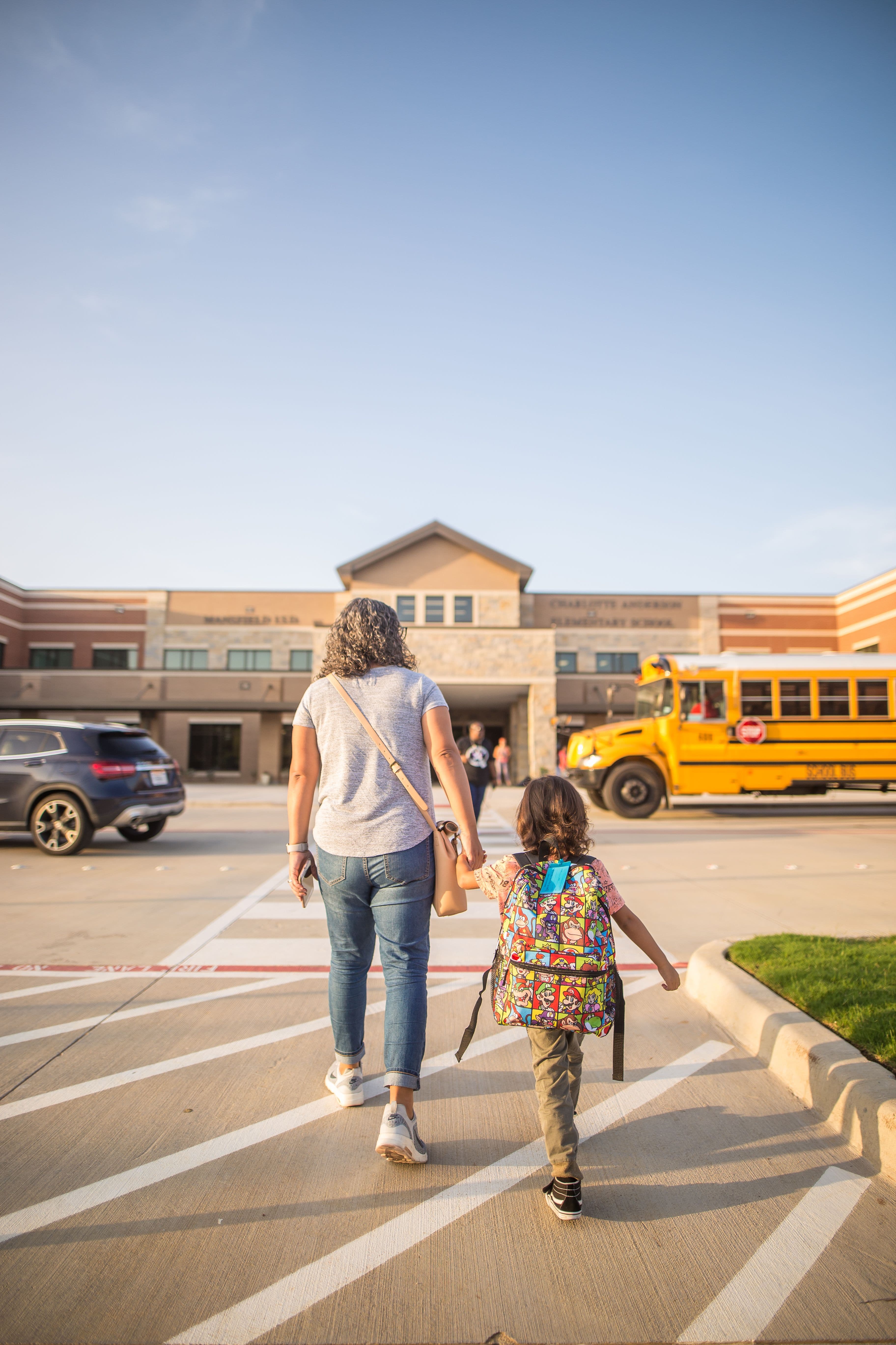 A parent holding a child's hand outside a school at pickup