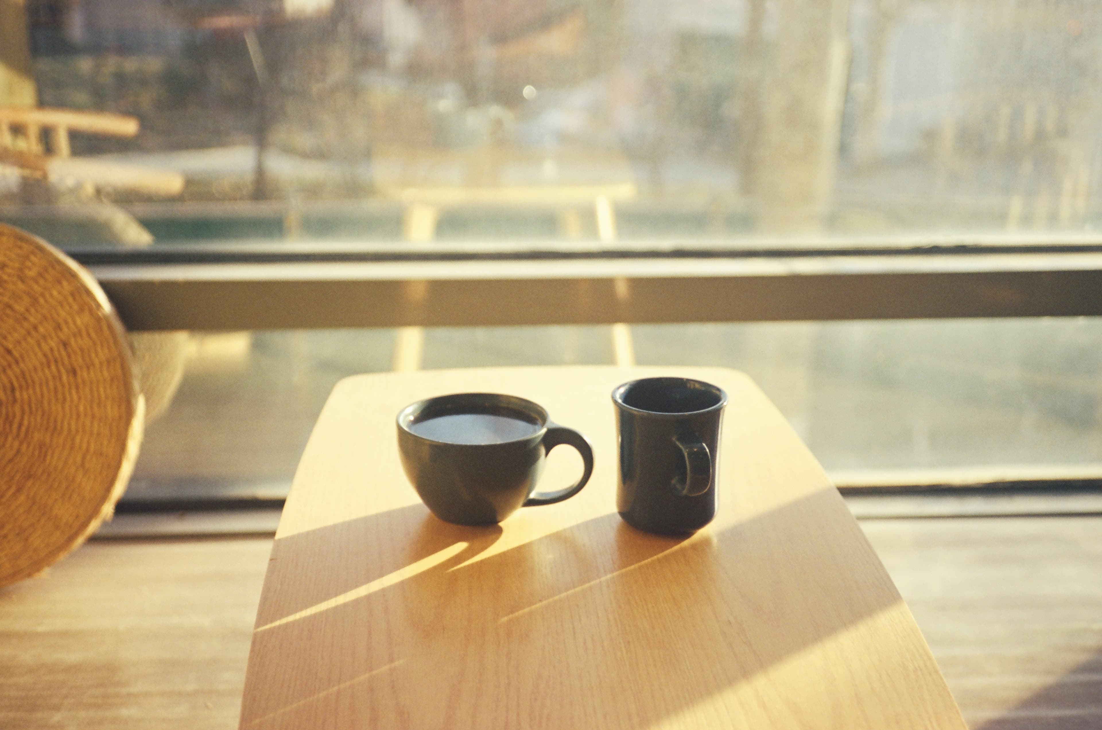 Two coffee mugs across a small wooden table in front of a window