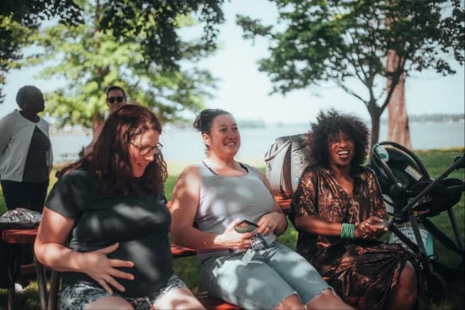 Three parents sitting together on a park bench, candid