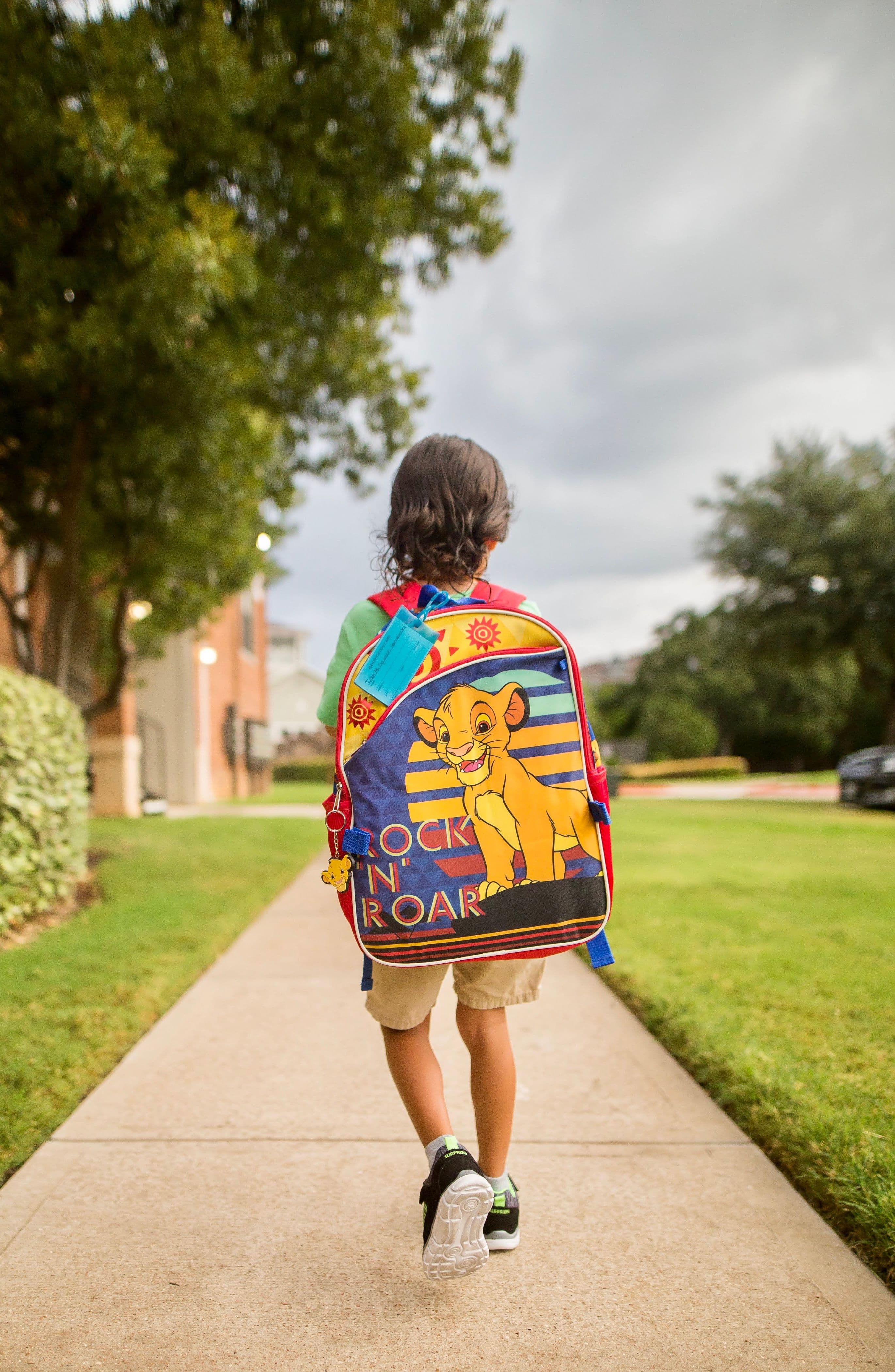 A child wearing a backpack walking along a quiet sidewalk